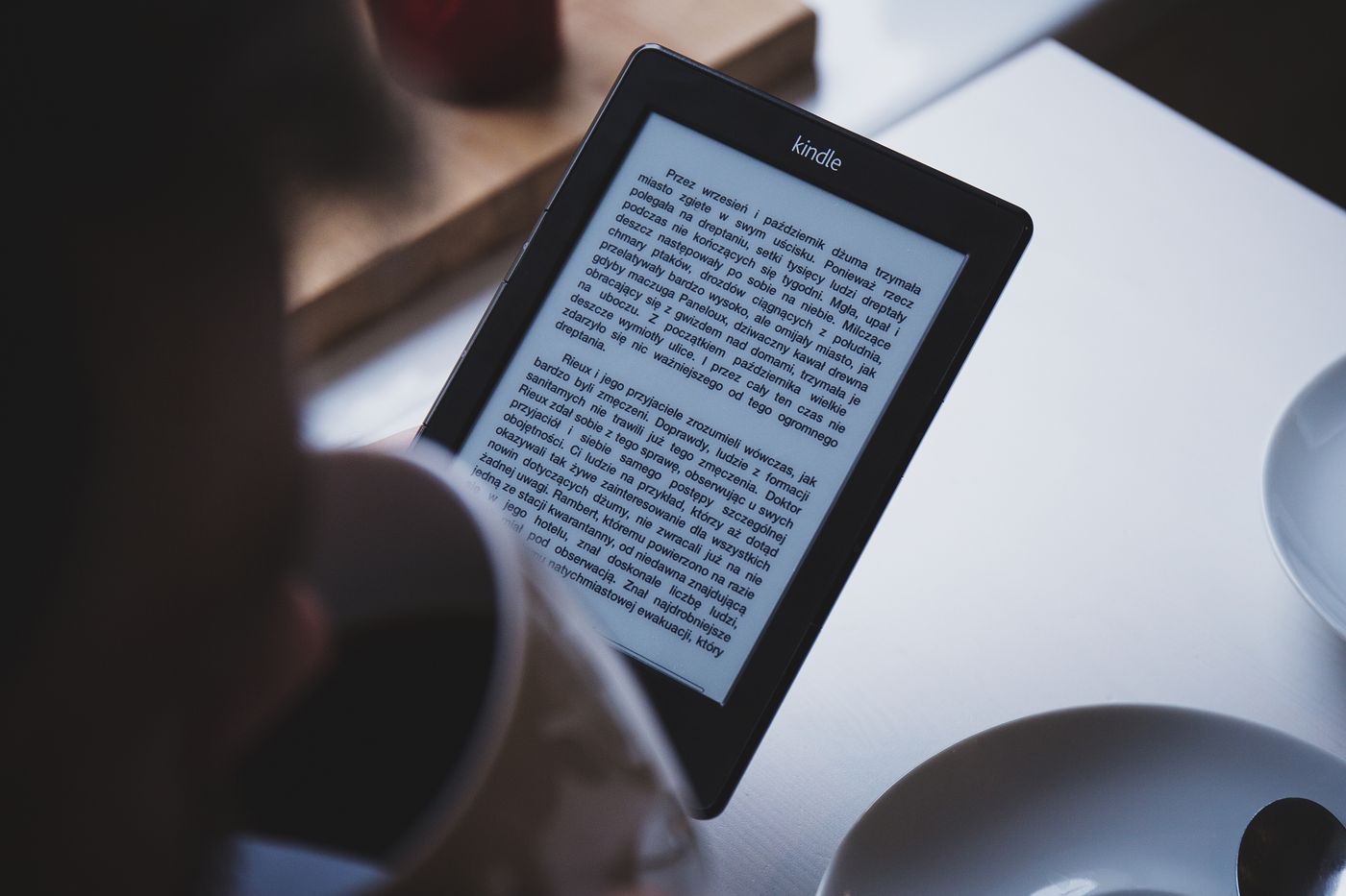 A person reading on a Kindle e-reader with a cup of coffee