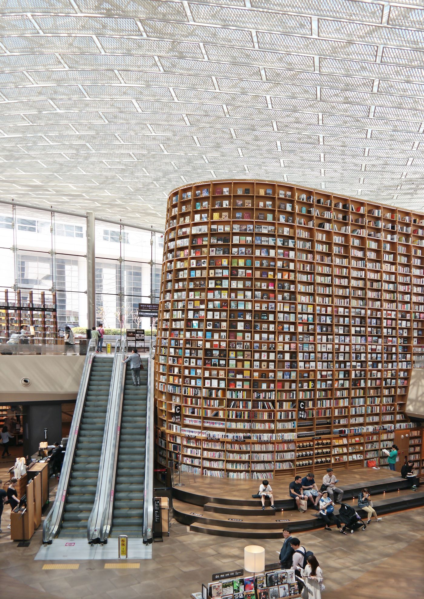 People reading and sitting beneath a towering curved wall of bookshelves