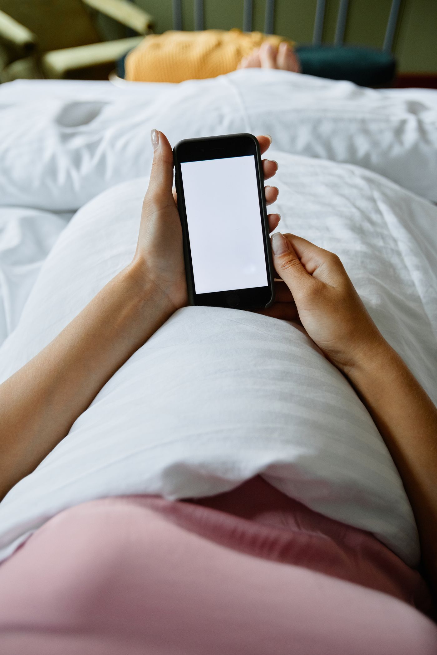 A person lying in bed holding a smartphone, its screen glowing